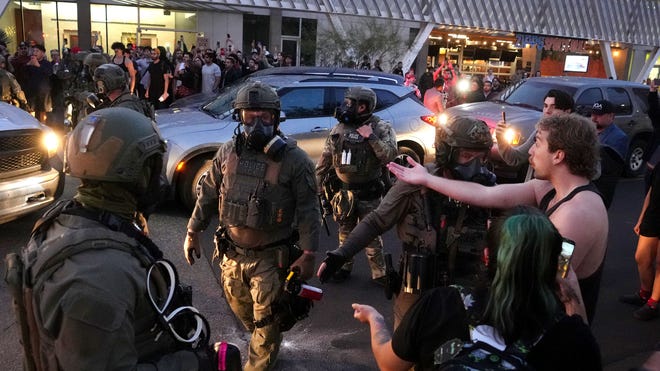 Tactical law enforcement personnel face off with protesters in a street standoff, illustrating local tensions over ICE and Border Patrol policies as Arizona lawmakers voted on new funding.