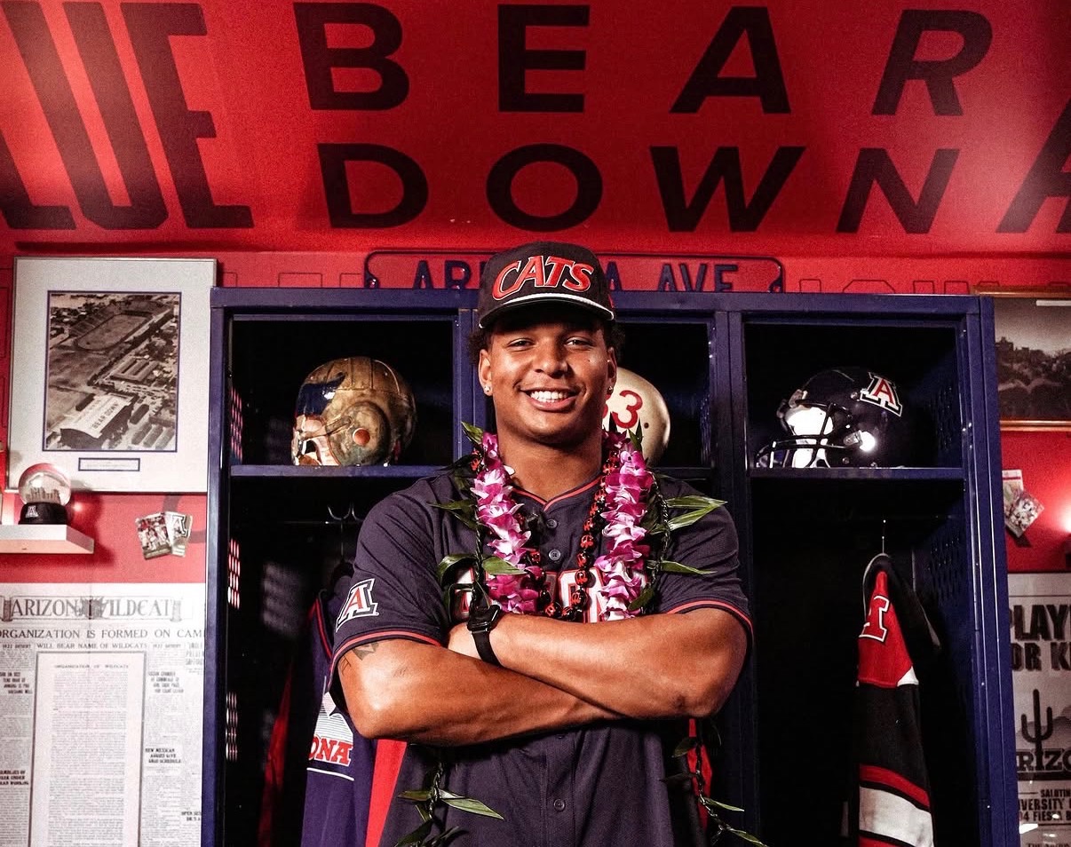 Locker-room introduction: the signee smiles wearing a 'CATS' cap and lei in front of Arizona lockers after announcing his commitment to the Wildcats program.