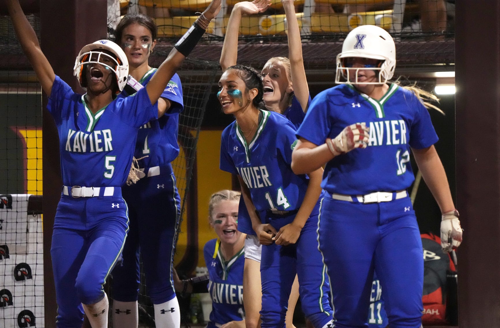Xavier teammates erupt in celebration in the dugout as they cheer on a play during a postseason/state tournament game.