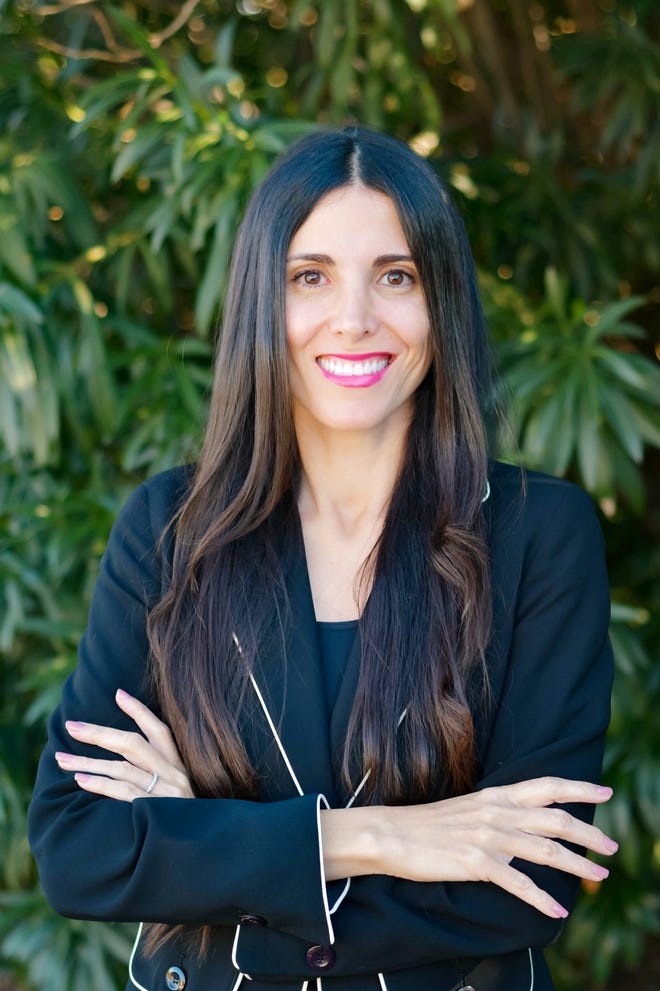 Campaign portrait of a candidate for Arizona superintendent, smiling with arms folded in front of foliage.