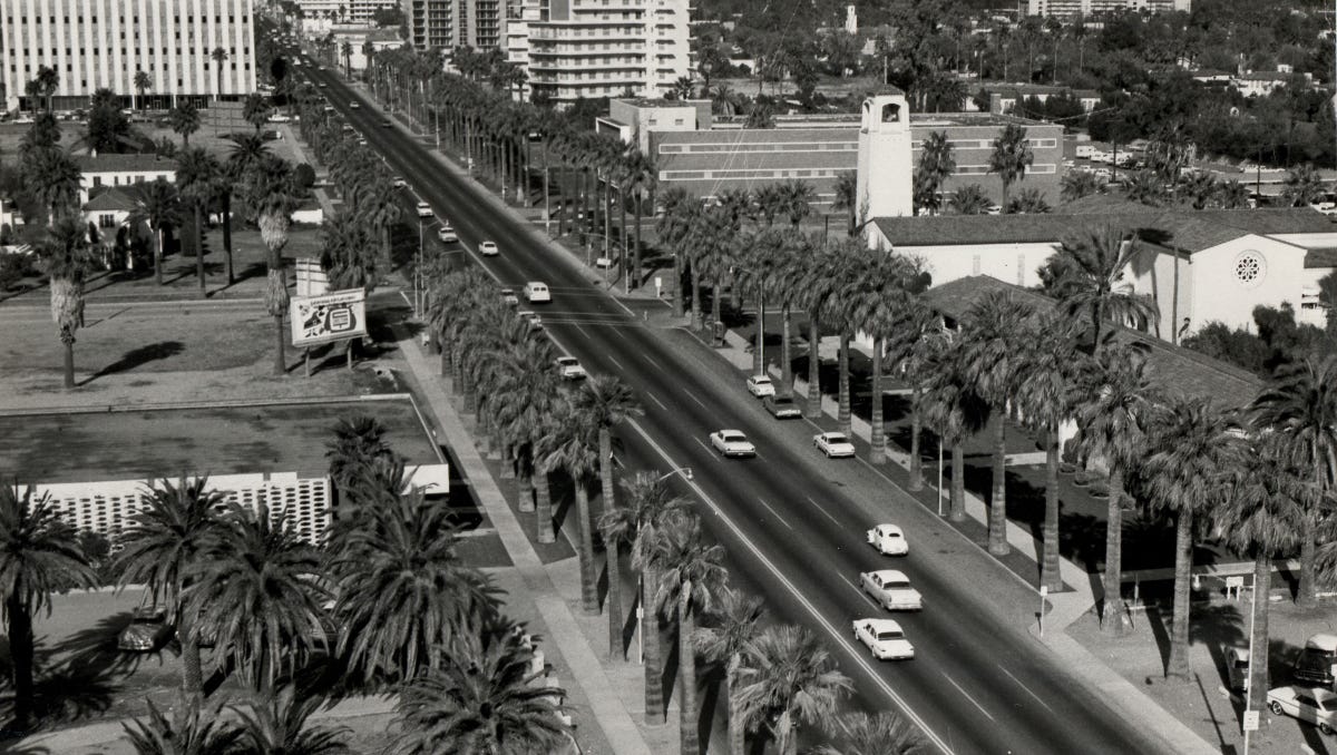 Historic aerial view of a palm‑lined Phoenix avenue with mid‑century cars — a snapshot of the older streets and eras whose naming histories are recounted in the article.