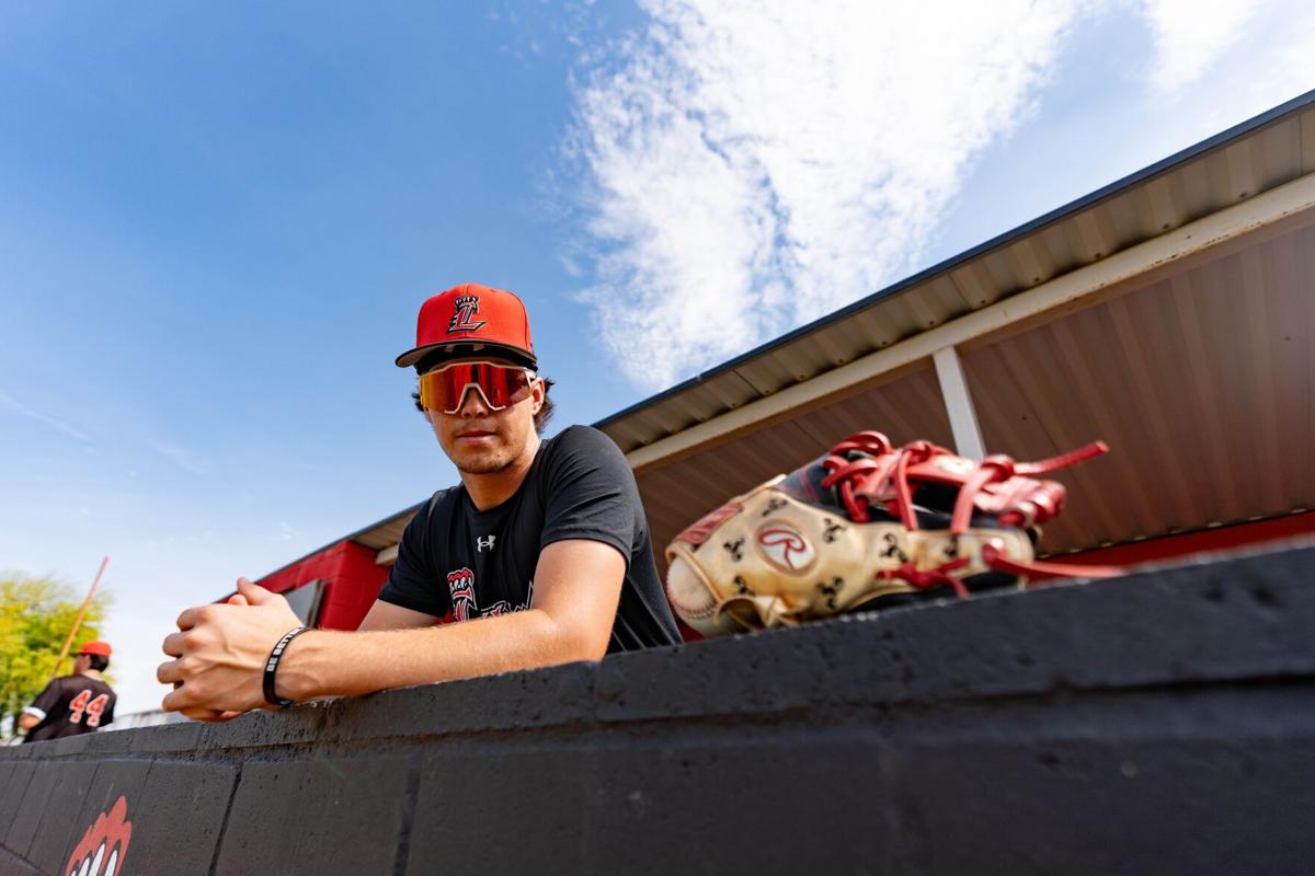The incoming Arizona Wildcat baseball signee during a practice, shown in Liberty baseball gear leaning on the dugout with his glove visible in the foreground.