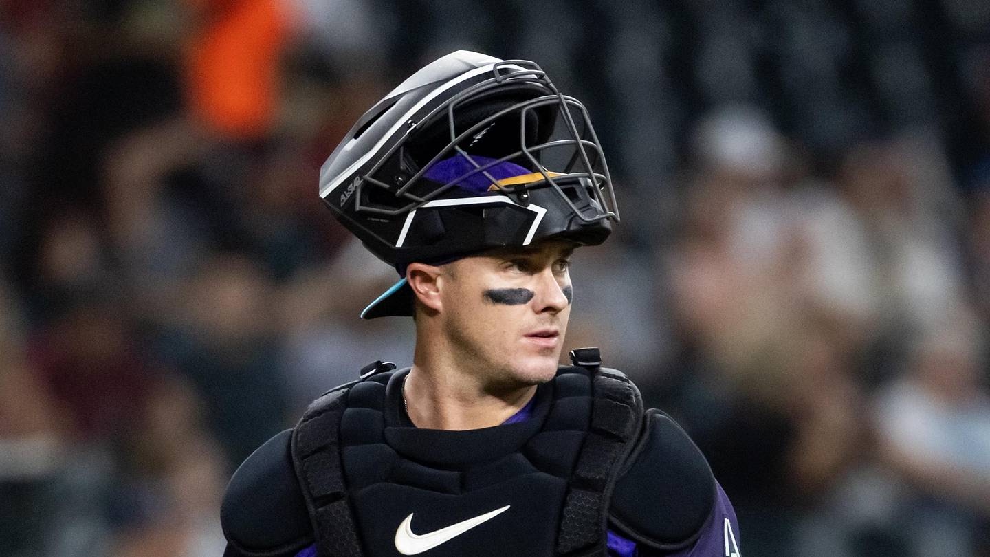 McCann in full catching gear with mask atop his helmet during a game, underscoring his defensive presence as he rejoins Arizona's catcher group.