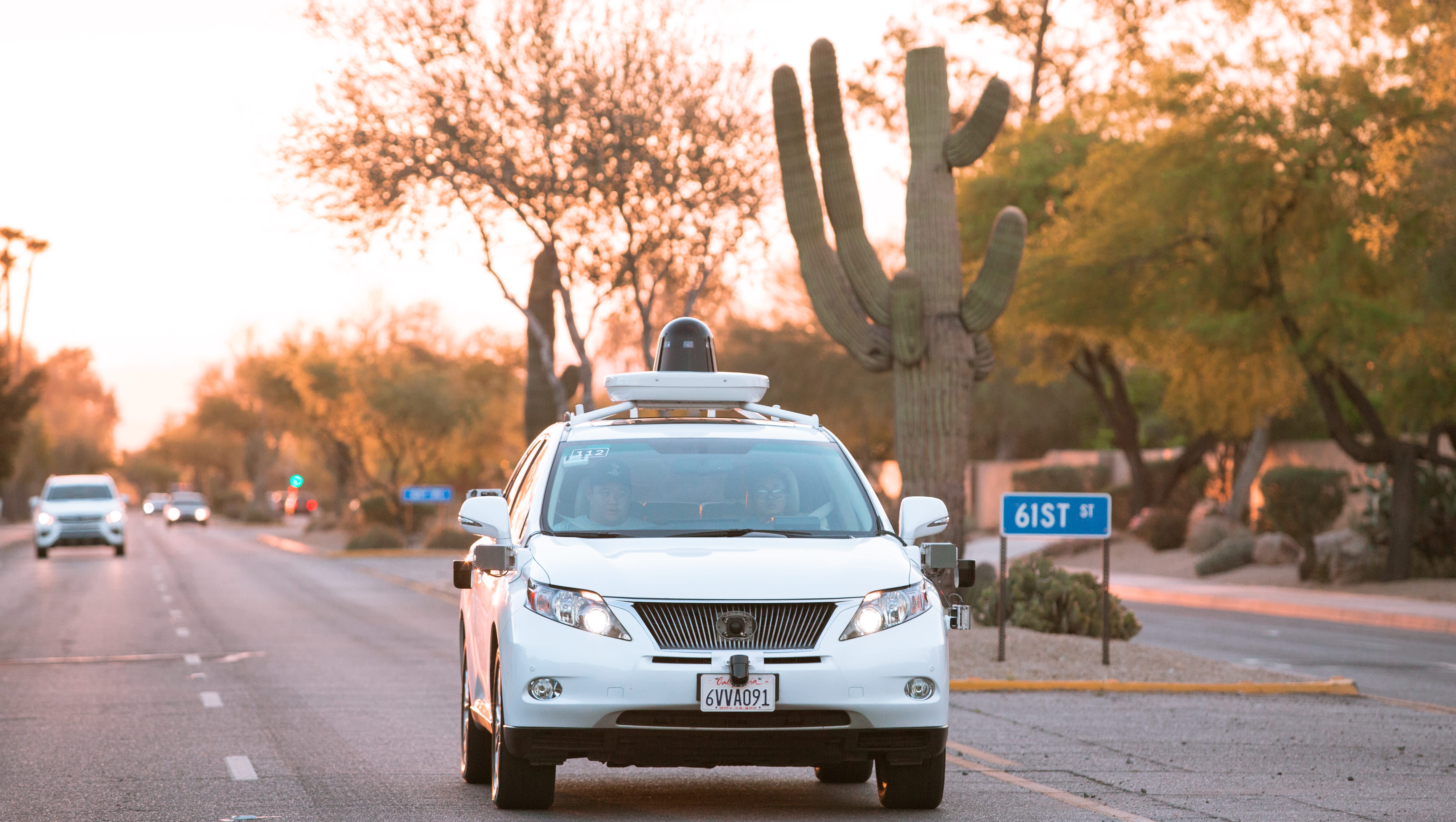 Waymo test vehicle on a Phoenix-area street near 61st Street, framed by desert landscaping — illustrating Waymo’s growing presence in Arizona.