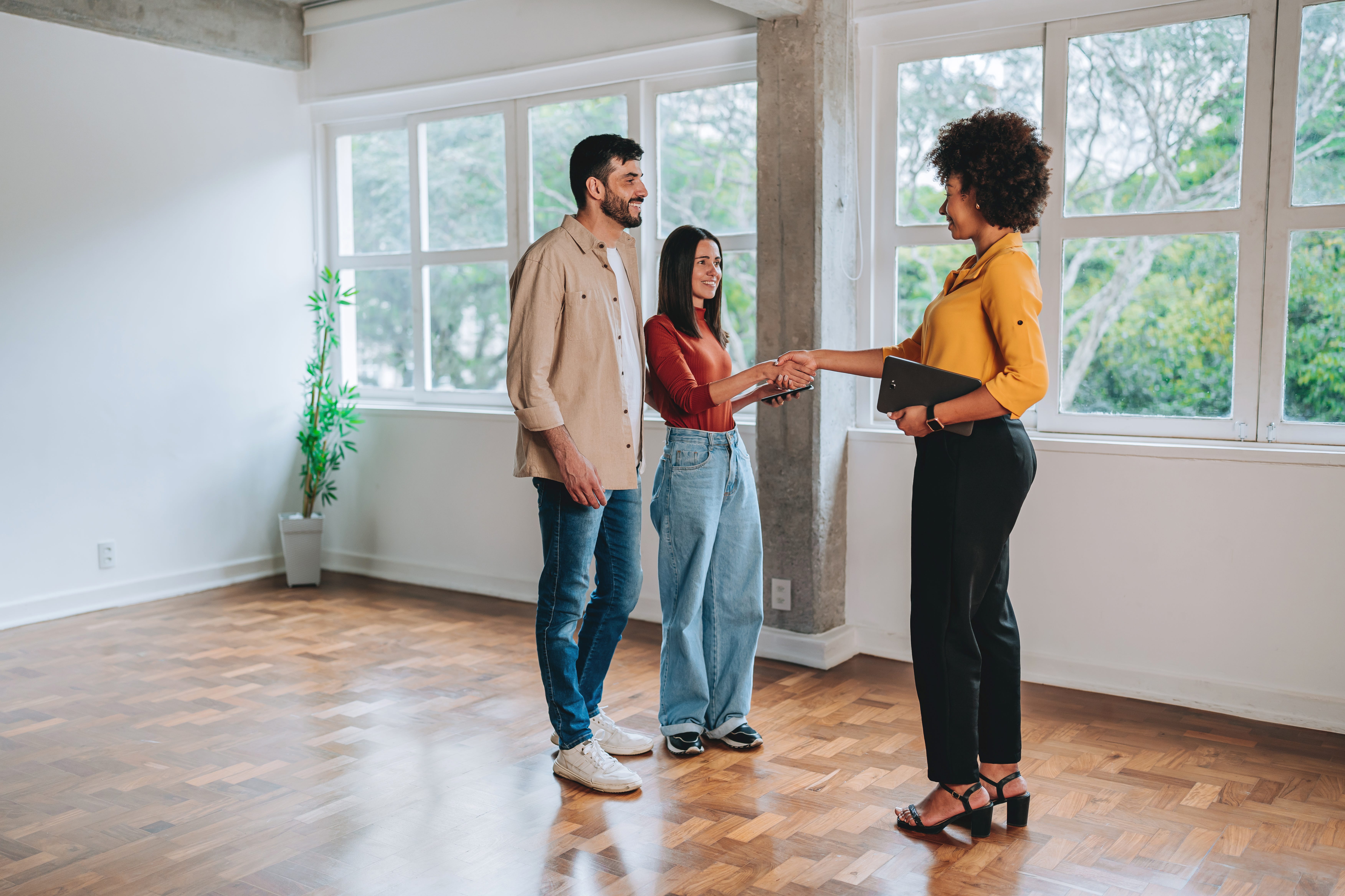 A real estate agent shakes hands with a couple during a home showing — the article reviews top home‑warranty providers Arizona buyers and owners can use to help cover repair costs.