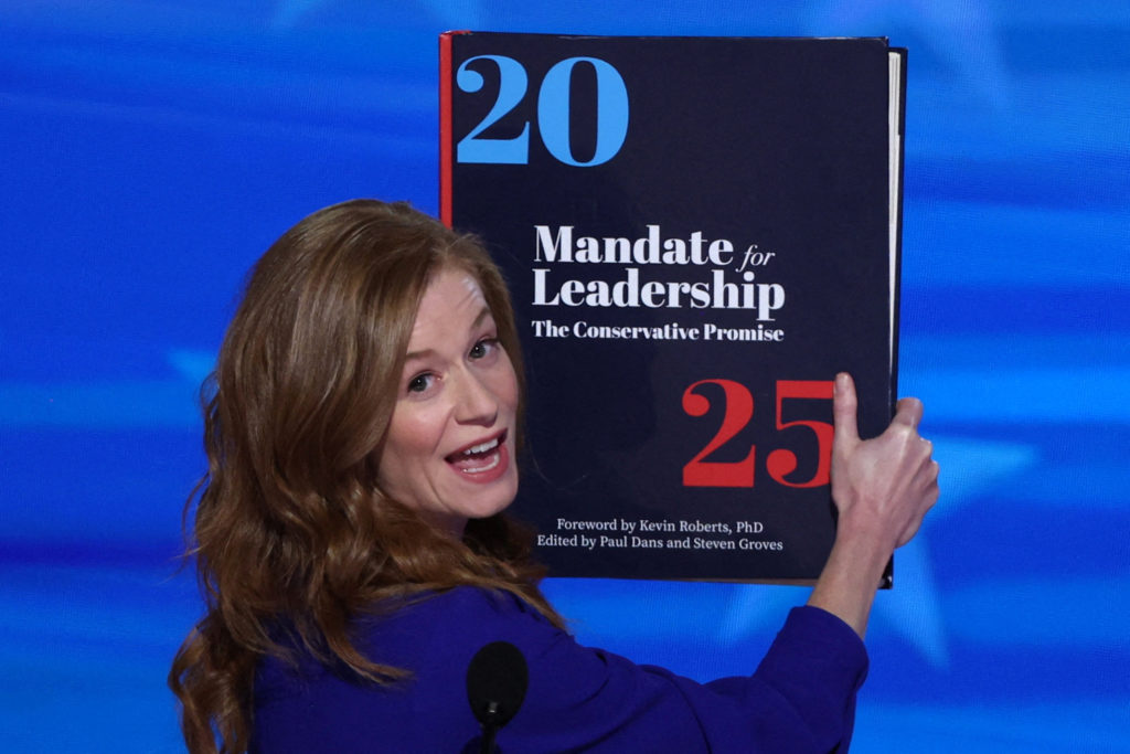 A presenter displays the 'Mandate for Leadership 2025' volume at a conservative event — the Project 2025 document shaping the policy debate Arizona Democrats are responding to.