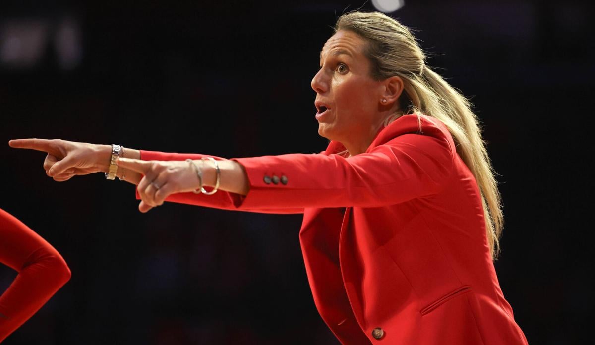 Sideline moment as a woman in a red blazer points and directs from the Arizona bench during a women's college basketball game.