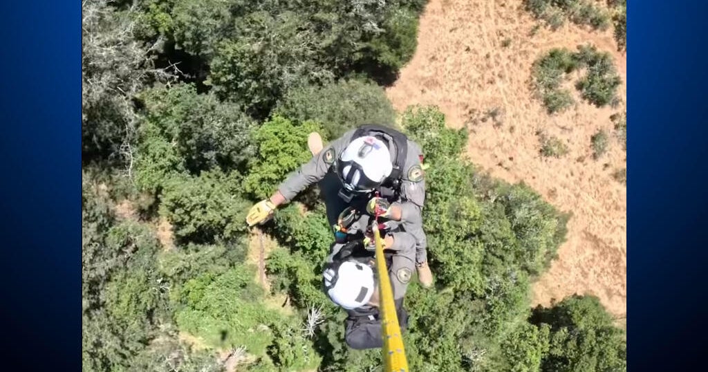 Shows: Aerial view of rescue personnel being hoisted over forested terrain during the operation that located the lost hiker at high elevation.