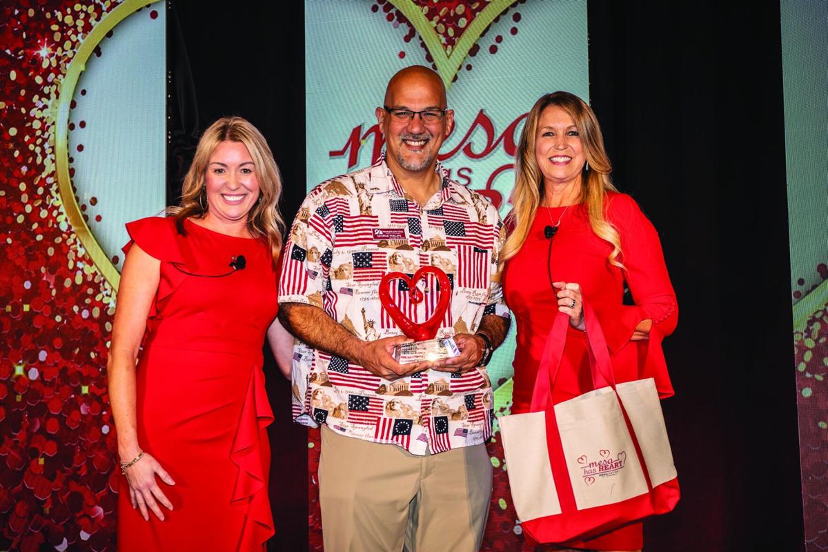 An award recipient holds a heart-shaped trophy flanked by two presenters onstage at the Mesa Chamber's 'Mesa Has Heart' awards gala.
