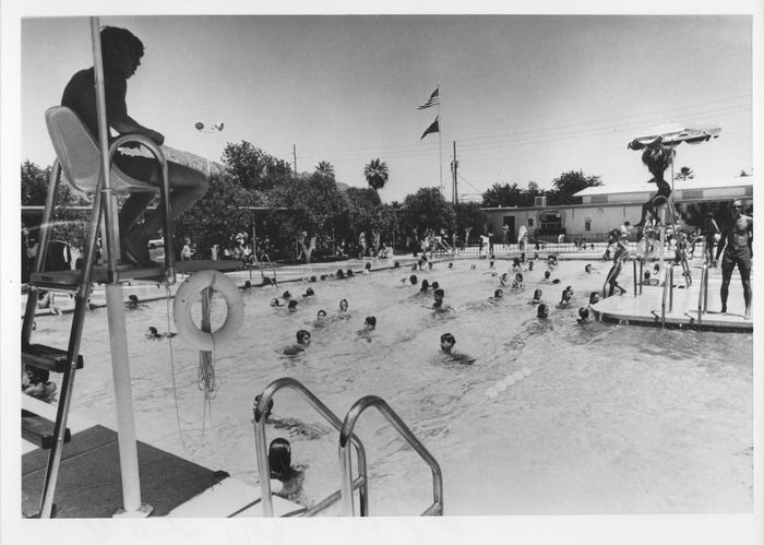 Mid-20th-century image of a busy public pool with a lifeguard chair and numerous swimmers, showing continued recreational use of Arizona's older pools.
