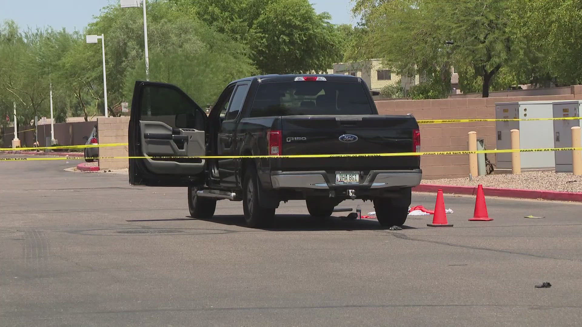 A Ford pickup with its door open sits behind yellow police tape and evidence cones at the Mesa crime scene near University Drive and Greenfield Road; a suspect was later arrested and booked.