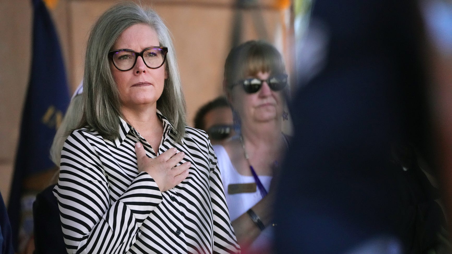 Shows: Gov. Katie Hobbs places her hand over her chest at a public event; Hobbs and GOP leaders agreed on an $18.29 billion budget that pauses data center subsidies and codifies federal tax cuts.