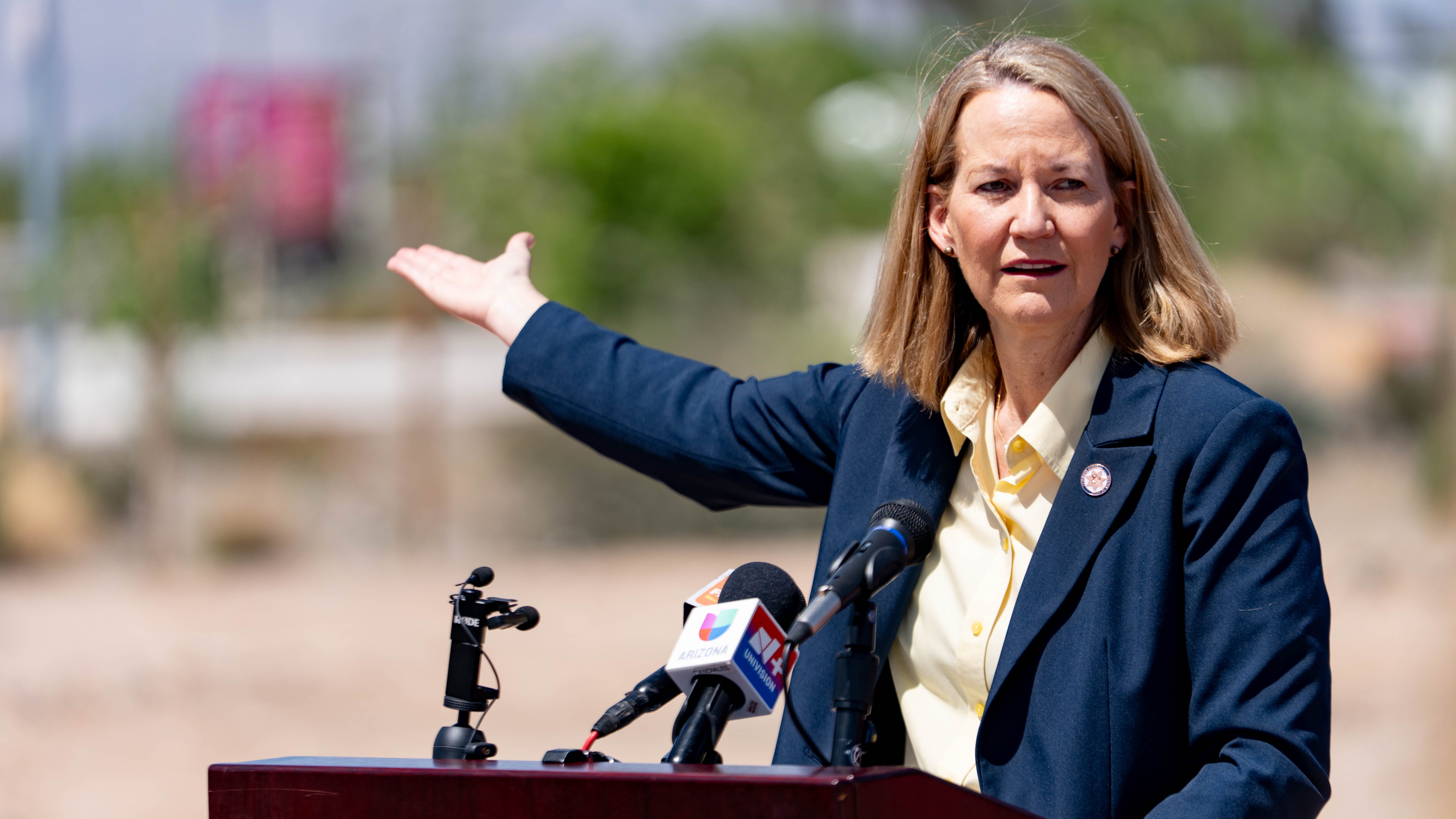 An Arizona official gestures during a news conference about the proposed ICE outpost, speaking in front of microphones from local media outlets.