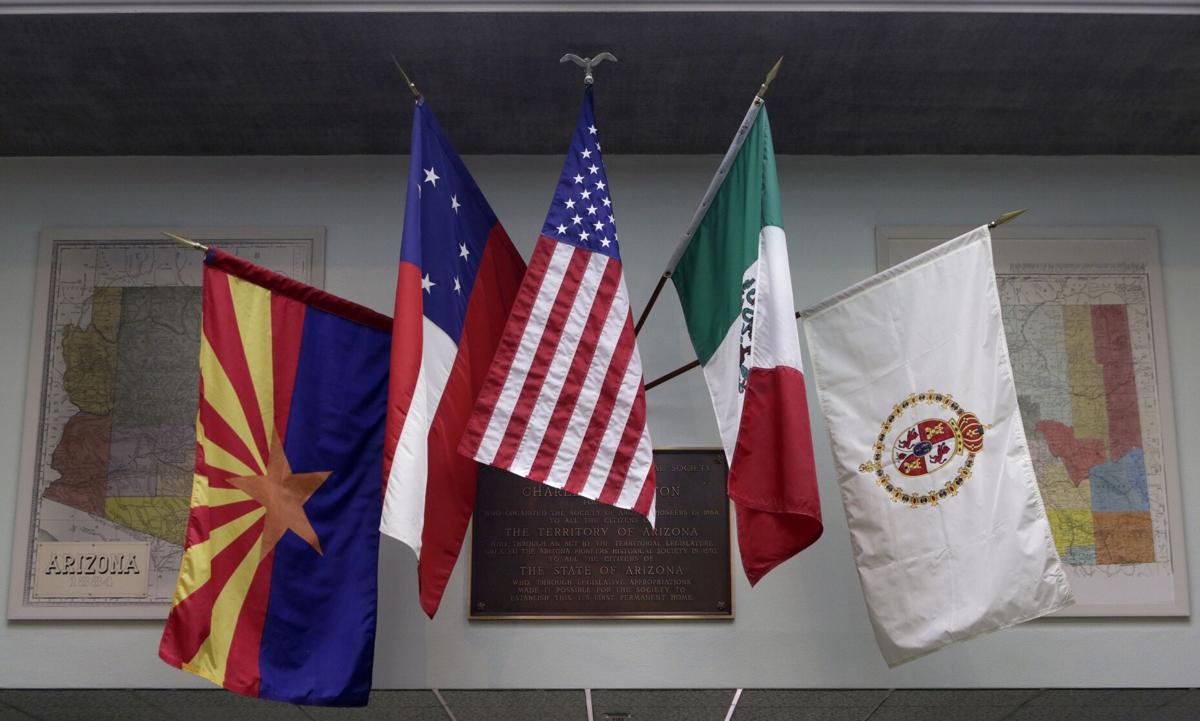 A display of historic flags — including the Arizona state flag, an early U.S. banner and a Mexican flag — mounted inside a Tucson venue, illustrating the region’s changing sovereignties.