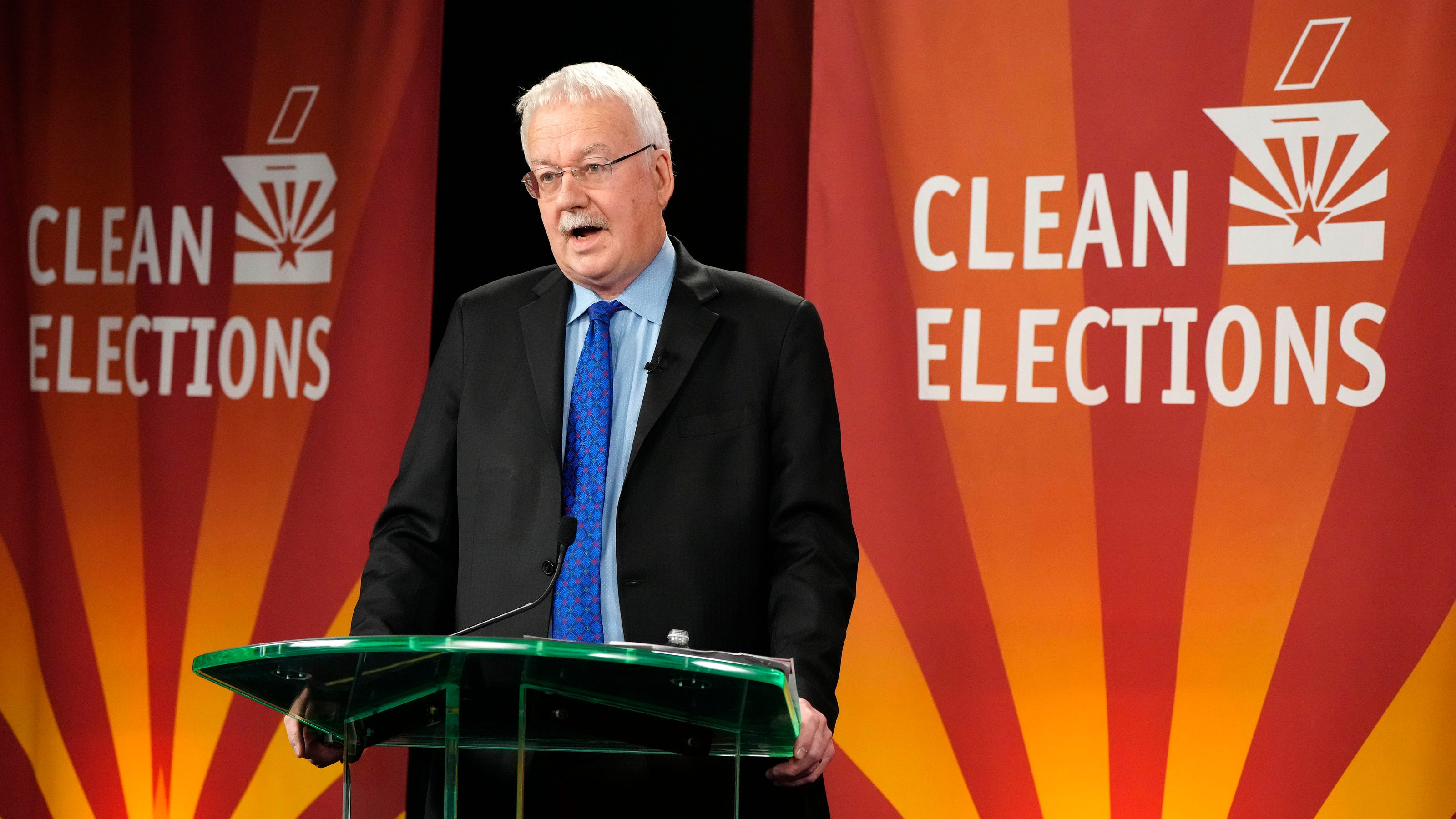 A candidate speaks from a podium with "Clean Elections" banners in the background during a debate in the northeast Valley primary race.
