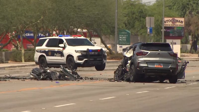 Debris and a mangled SUV remain in the street while a police SUV blocks the scene on Buckeye Road in west Phoenix after a fatal crash involving semitrucks.