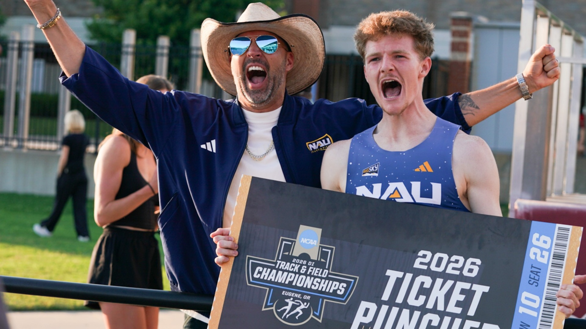 A NAU coach and runner celebrate while holding a large 'Ticket Punched' board, marking the team's qualification for the 2026 NCAA Outdoor Track & Field Championships.