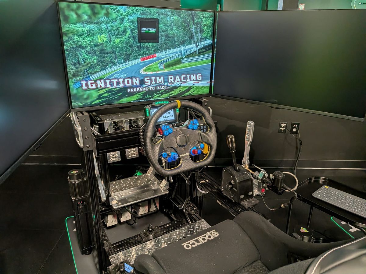 An Ignition Sim Racing cockpit at the Tucson location with the venue's welcome screen and professional wheel, pedals and shifter ready for drivers.