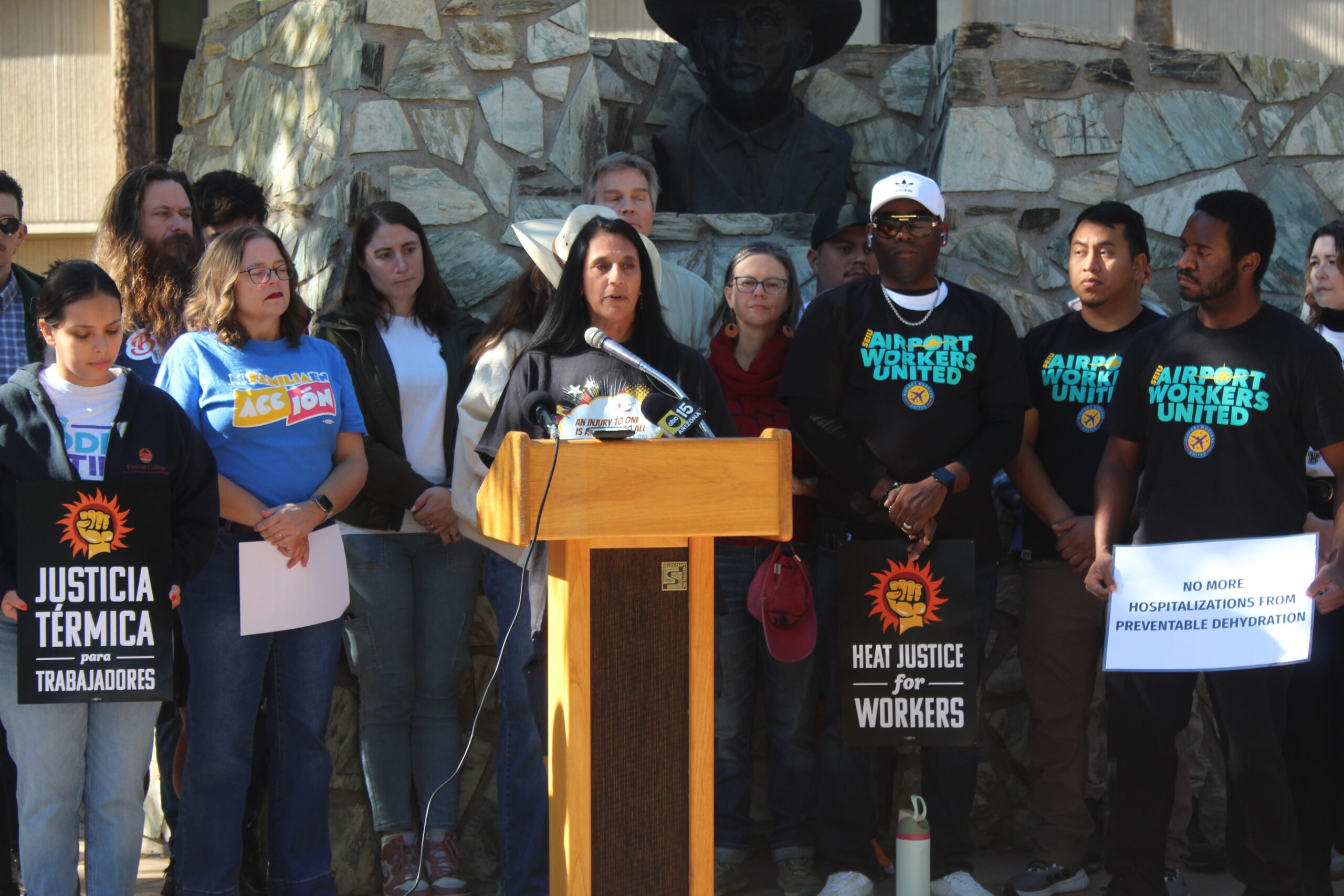 Community members and workers stand at a press podium holding 'Heat Justice' signs, calling for stronger protections and water access for farmworkers facing rising temperatures.