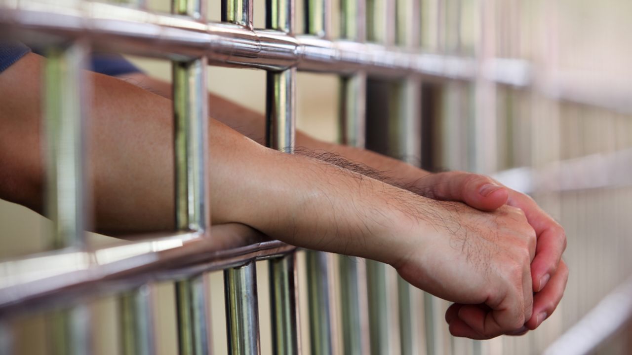 Hands gripping jail cell bars, illustrating the 28-year prison term handed down in the case.