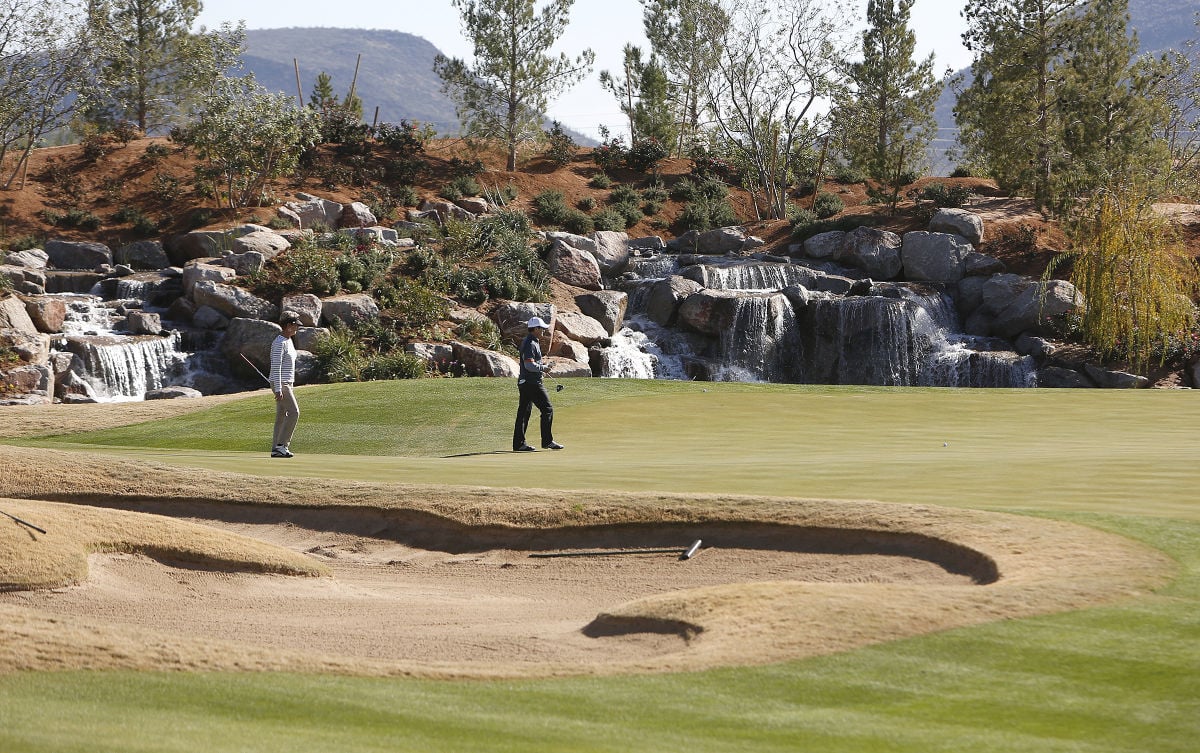Players walk the putting surface at Sewailo Golf Club with rock-lined waterfalls and bunkers visible on the course.