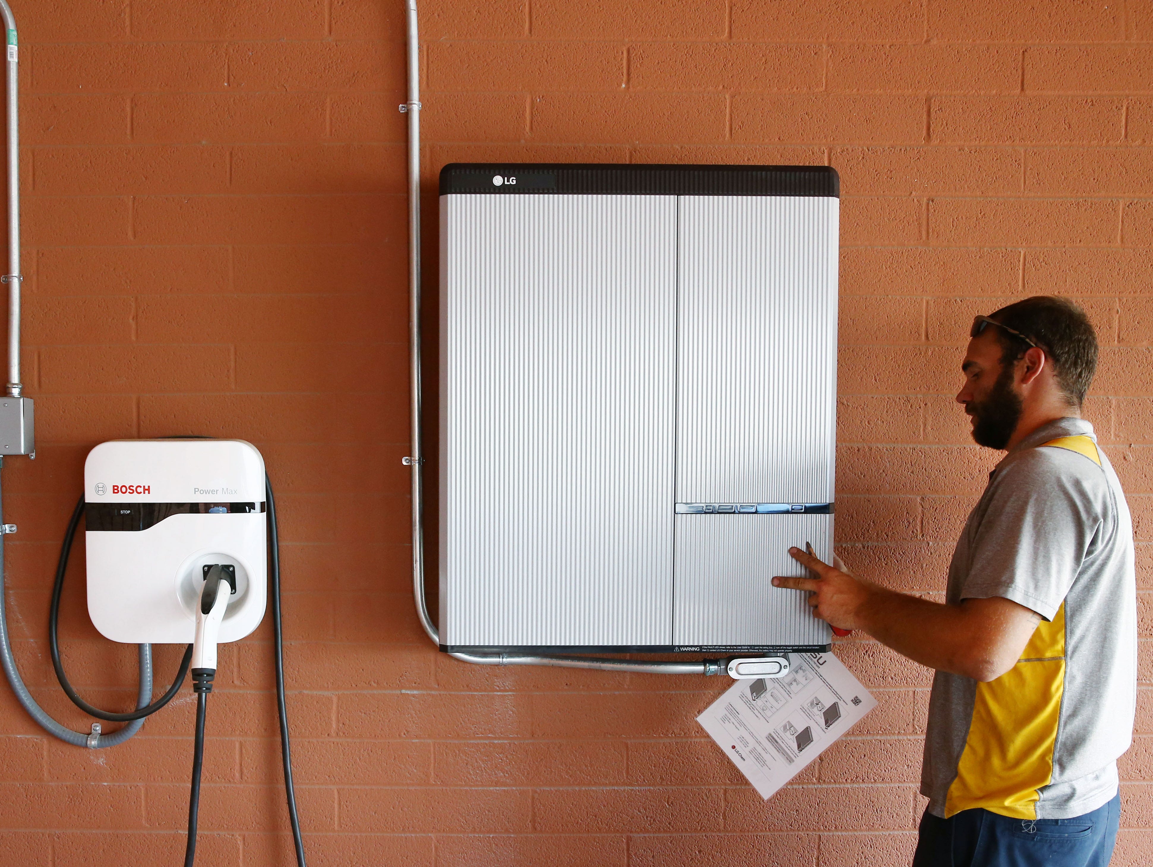 A residential energy storage cabinet (LG) and EV charger being inspected by a technician — an example of home battery systems that store solar power to help reduce utility costs.