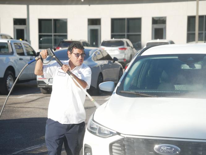 A Jim Click Automotive team member washes a vehicle on the dealership lot; the company earned national recognition for expanding inclusive hiring and job-training programs.