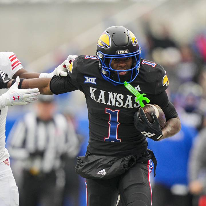 Kansas ballcarrier powering through contact in Jayhawks black uniform — a game-action shot representing the prospect whose path to playing time could be affected by Seattle's trade for Irvin Charles.